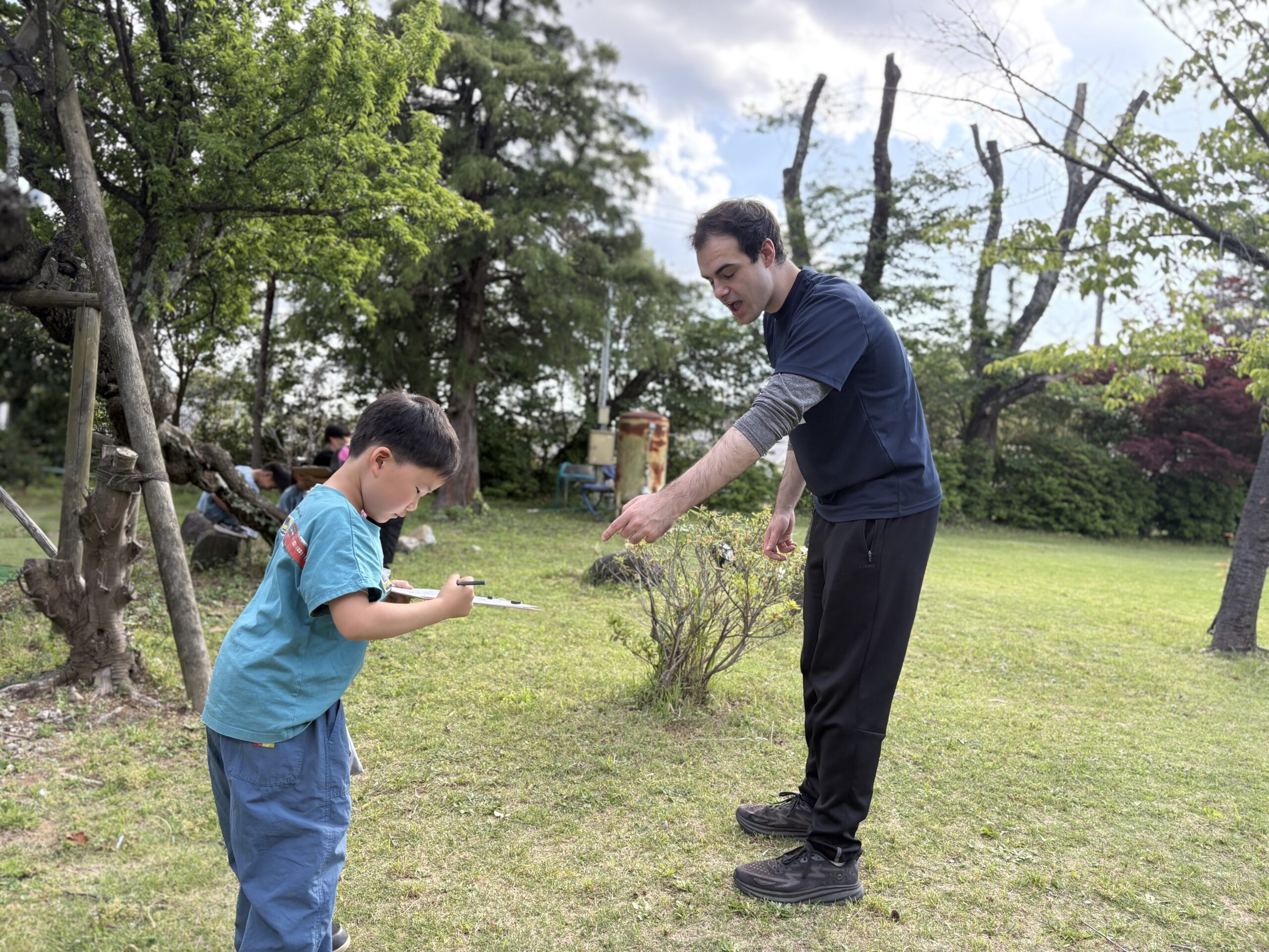 緑の園庭で先生と活動する子ども